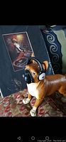 Boxer dog figure with black headphones in front of framed DJ print on patterned surface