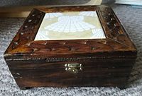 Closed view of vintage wooden box for domino set with carved frame design and decorative tile inlay on lid