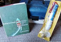 Fishing related items including a boating book, sealed boat speedometer, and closed blue tackle box.
