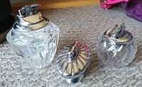 Set of three vintage table lighters shown on carpet, featuring clear cut glass or crystal bases with chrome ignition tops.