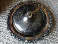 Top-down view of the tarnished covered serving platter showing ornate edge detail and knob handle on lid