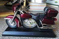 Side view of the star motorcycle clock showing the clock embedded in the motorcycle body, maroon paint, black seat, chrome details, and black base.