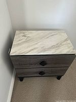 Close-up image of one night table showing faux marble top and wood grain body with black diamond-shaped drawer pulls