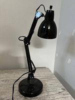 Black extendable desk lamp on a wooden surface against a plain wall.