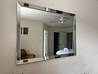 Front view of rectangular mirror reflecting part of a room with a ceiling fan and doorways.