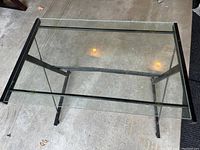 Top view of a rectangular glass coffee table with a black metal frame on a concrete floor.