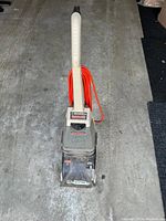 Full view of Hoover SteamVac commercial carpet cleaner showing the white handle and orange power cord coiled around it. Machine appears intact but used.