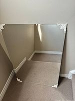 Clear image of square mirror leaning against wall showing detailed decorative metal corner pieces and reflection of carpet and baseboards.