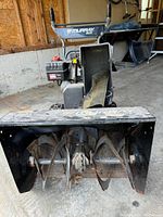Front view of the snowblower showing the auger blades inside the housing and the gas engine behind it.