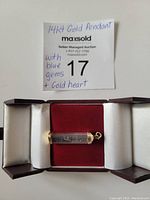 Front view of the 14kt yellow gold pendant with the transparent case showing blue gemstones and a gold heart inside, presented on red velvet.