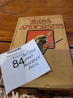 Front cover of the antique book titled 'Tales From Hans Andersen' showing beige cloth cover with printed title and illustration of a figure with a hat and sword.