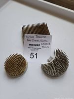 Photo of three antique Japanese pin frogs made of metal, including one round and two segment shaped frogs with sharp metal pins for flower arranging.