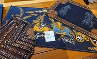 Image showing folded batik cotton table napkins with brown and white patterns alongside table runner and place mats with horse and rider batik design.