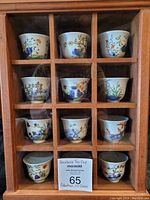Twelve hand-painted porcelain tea cups in a wooden display case