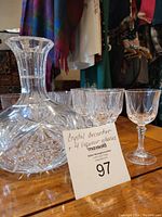 Clear crystal decanter and four liquor glasses arranged on wooden surface with auction card in front.