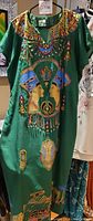 Full front view of a green traditional Egyptian dress decorated with colorful sequins and beads arranged in symbolic and ornamental patterns.