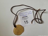 Photo of the gold dipped leaf pendant laid flat with brown leather strap extended, showing shape and texture of the pendant and strap details.