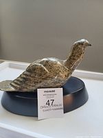 Side view of the carved granite loon sitting on black stand, showing overall shape and stone texture.