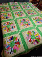 Full view of the bedspread displayed on a bed, showing the full pattern with hand-stitched floral blocks and contrasting green grid borders.