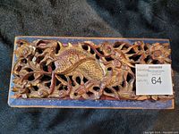 Full view of the front of the carved wooden wall hanging showing the dragon and surrounding decorative elements with a visible auction sticker.