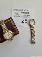 Photo of both ladies' watches, Citizen with rhinestone bezel and Cardinal with elastic band visible, laid on a white background near the lot tag.