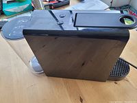 Side view of black Nespresso Mini coffee maker showing water reservoir and drip tray assembly.