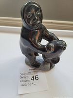 Front view of black soapstone carving showing Eskimo figure holding a seal with handwritten lot note.