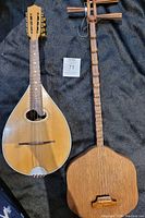Both traditional Asian string instruments laid flat on a black cloth background, showing front of the mandolin-style and long-necked instrument with carved tuning pegs.