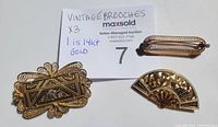 Three vintage brooches displayed together with a MaxSold note stating 1 is 14kt gold.