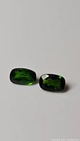 Two cushion cut deep green chrome diopside gemstones shown on white background clearly displaying their color and clarity.
