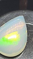Close-up photo of pear-shaped Ethiopian opal cabochon gemstone showing bright green and yellow internal flashes under light.
