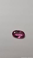 Oval faceted bubble gum pink tourmaline gemstone on a white background, showing the stone's color and clarity.