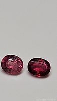 Two oval-shaped natural tourmaline gemstones shown on a neutral background with good focus on color and clarity.