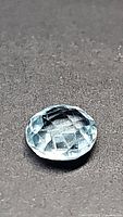Close-up photo of a 7mm natural sky blue topaz gemstone showing its double-sided round checkerboard cut and clarity.