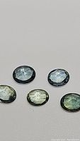 Five natural fancy multicolored sapphires with rose cut placed on a flat surface showing various colors including blue and green.