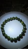 Top view of the stretchy green jade bead bracelet laid in a circle, showing color variations and bead quality.