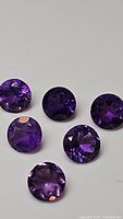 Photo showing six round faceted deep purple amethyst gemstones arranged on a white background