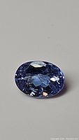 Close-up photo of natural tanzanite gemstone showing oval cut and color under neutral background.