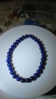 Top view showing the full circular arrangement of 24-26 polished, deep blue, spherical Lapis Lazuli beads on an elastic band.