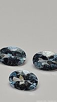 Three natural oval cut sky blue aquamarine gemstones clearly showing faceting and color under neutral lighting.