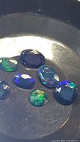 Seven natural Ethiopian black opal gemstones displayed on a dark base, showing bright and vibrant colors of blue, green, and rainbow hues under direct light.