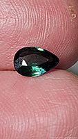 Close-up photo showing a pear shaped blue green sapphire held between fingers, highlighting size and color under light.