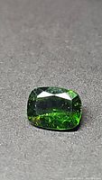 Close-up photo of a cushion-cut electric green chrome diopside gemstone showing facets and natural inclusions.