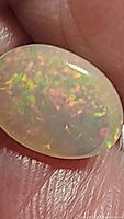 Close-up image showing the oval natural untreated Ethiopian opal held between fingers, displaying vibrant play of color.