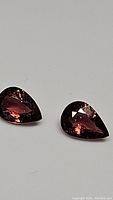 Two pear shaped hot pink tourmaline gemstones viewed close-up on a white background showing color and cut details.