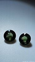 Pair of round-cut natural African sapphires displayed side by side, showing deep greenish-blue color and faceted surface, one photo angled with light reflection
