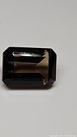 Close-up of a rectangular emerald cut smokey quartz gemstone with visible facets and deep brown color.