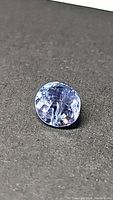Oval-shaped blue purple tanzanite gemstone laying on a dark surface, showing facets and color under light.