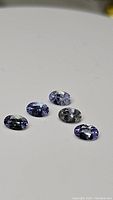 Four oval cut natural tanzanite gemstones shown on a white background, displaying purple blue hues and faceted cuts.