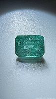Photo of a natural emerald cut green gemstone with visible inclusions from Zambia, backlit to highlight internal clarity and facets.
